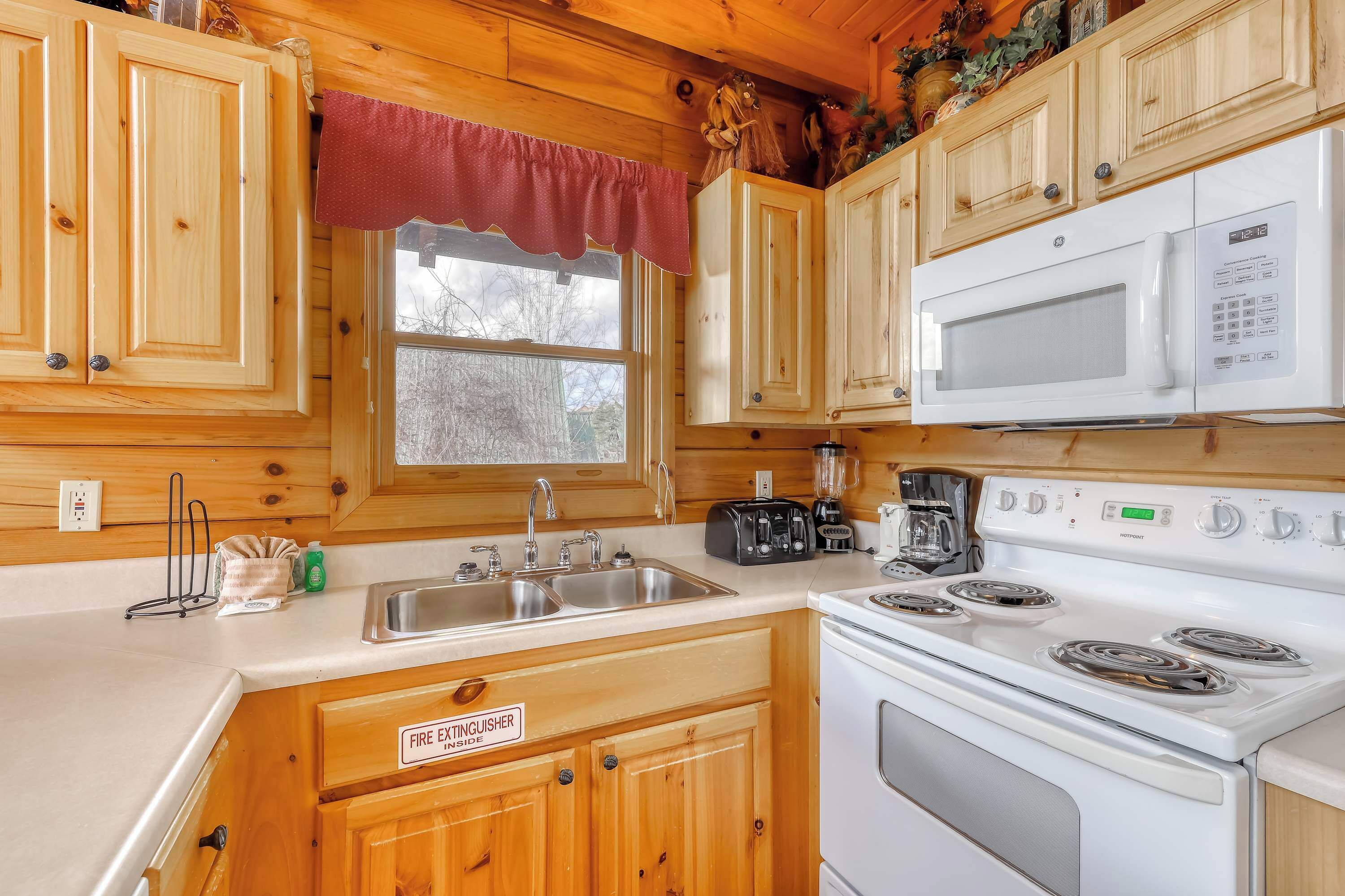 A compact kitchen with wooden cabinets, a white microwave, a stove, and a sink.