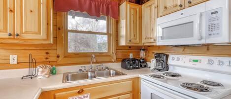 A compact kitchen with wooden cabinets, a white microwave, a stove, and a sink.