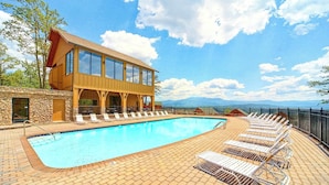 A swimming pool with lounge chairs, a wooden building with large windows, and a stone wall. - Cabin W Amazing Views・Hot Tub・Shared Sauna - Pool (Pigeon Forge)