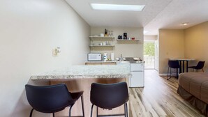 Una cucina compatta con isola centrale, sgabelli da bar, forno a microonde e macchina del caffè.