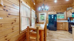Interior d'una cabana de fusta amb taula de menjador, cadires, nevera i armaris de fusta.