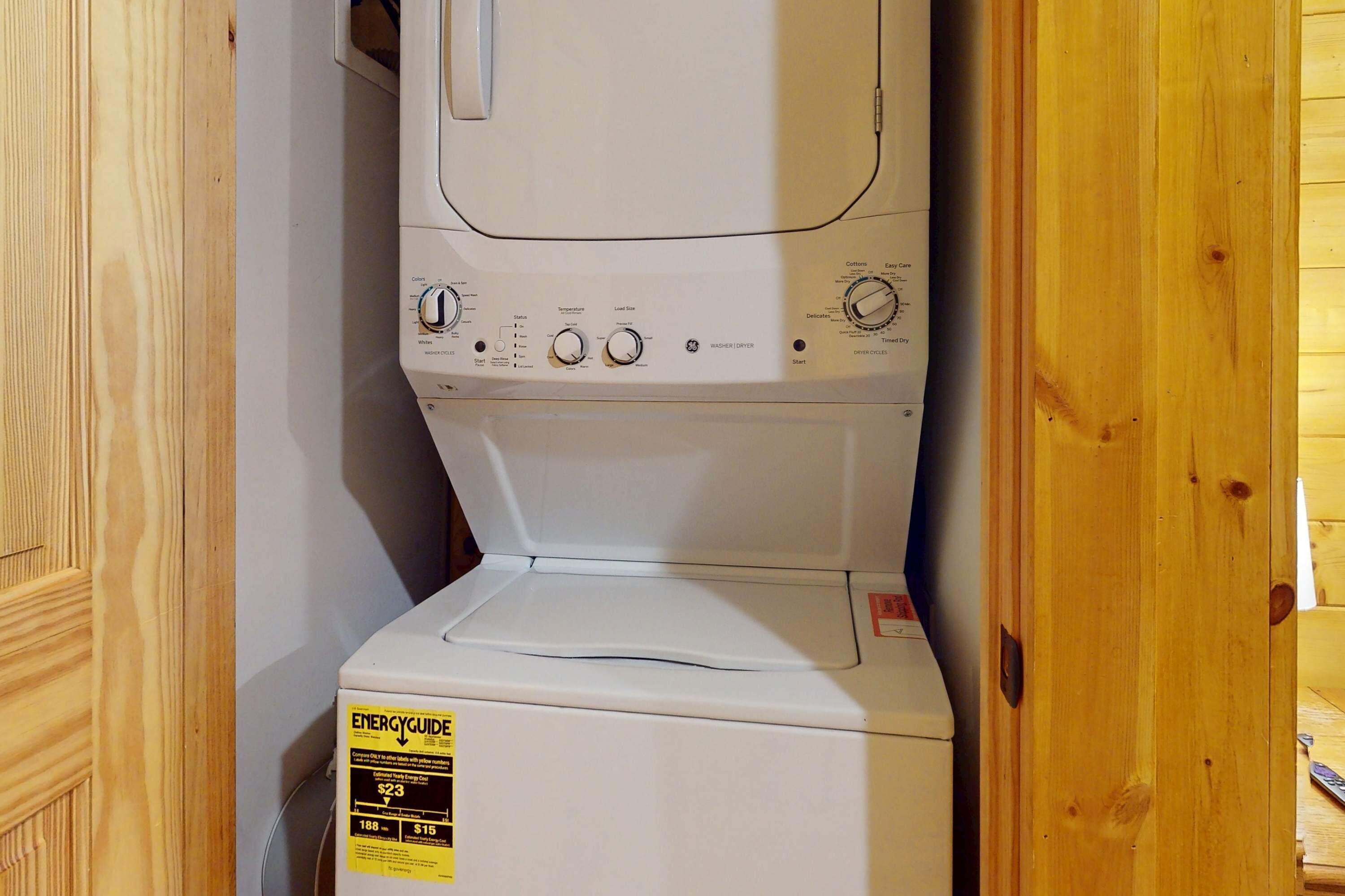 A compact washer and dryer unit with a control panel, a yellow energy efficiency label, and a wooden door frame.