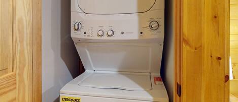 A compact washer and dryer unit with a control panel, a yellow energy efficiency label, and a wooden door frame.