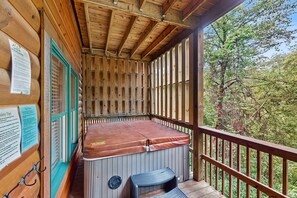 Eine Holzhütte mit Whirlpool, einer Holzterrasse und Blick auf Bäume.