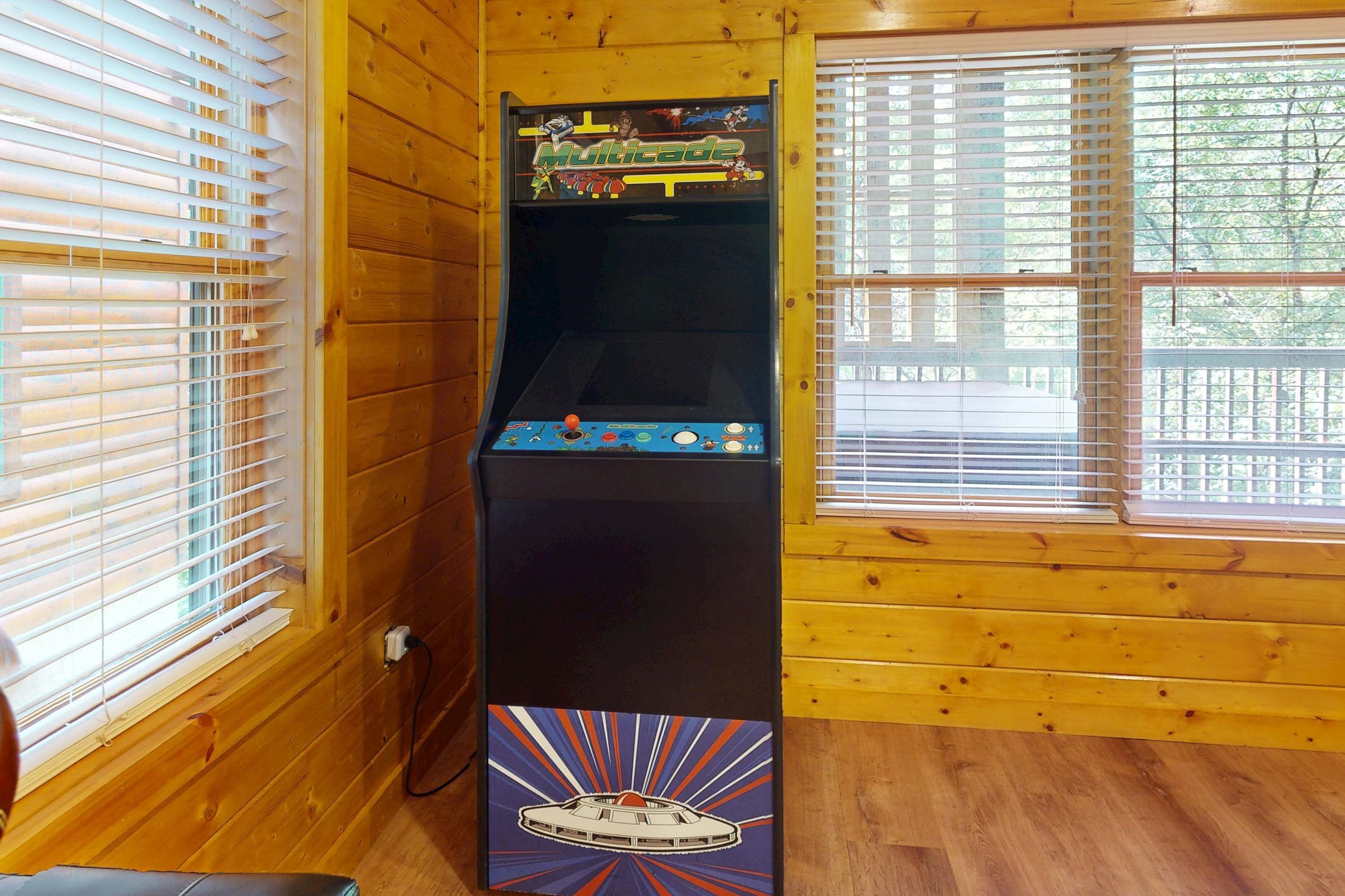 A wooden-paneled room with a vintage arcade machine labeled "Multicade" and a UFO-themed game.