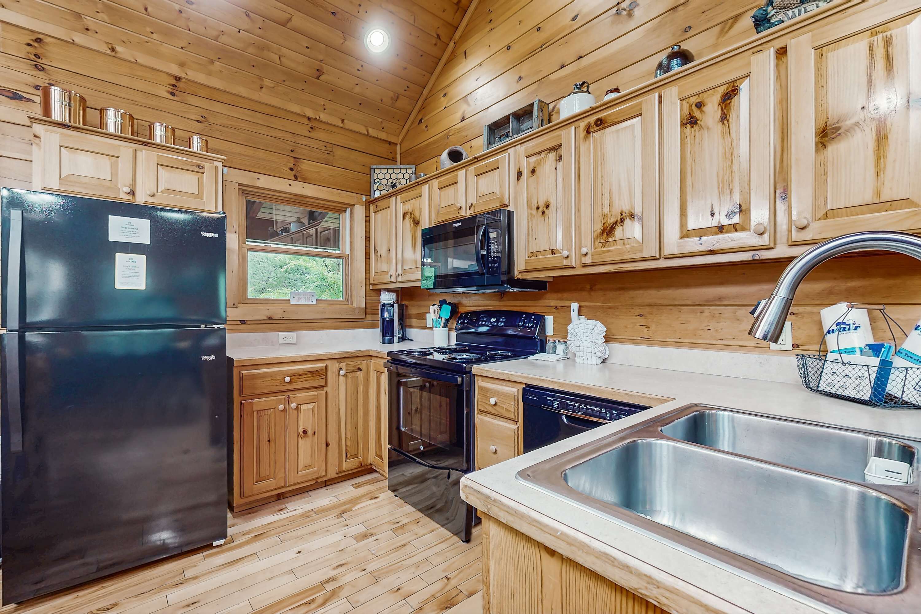 Una cocina con armarios de madera, un refrigerador negro, un microondas, una estufa y un lavabo.
