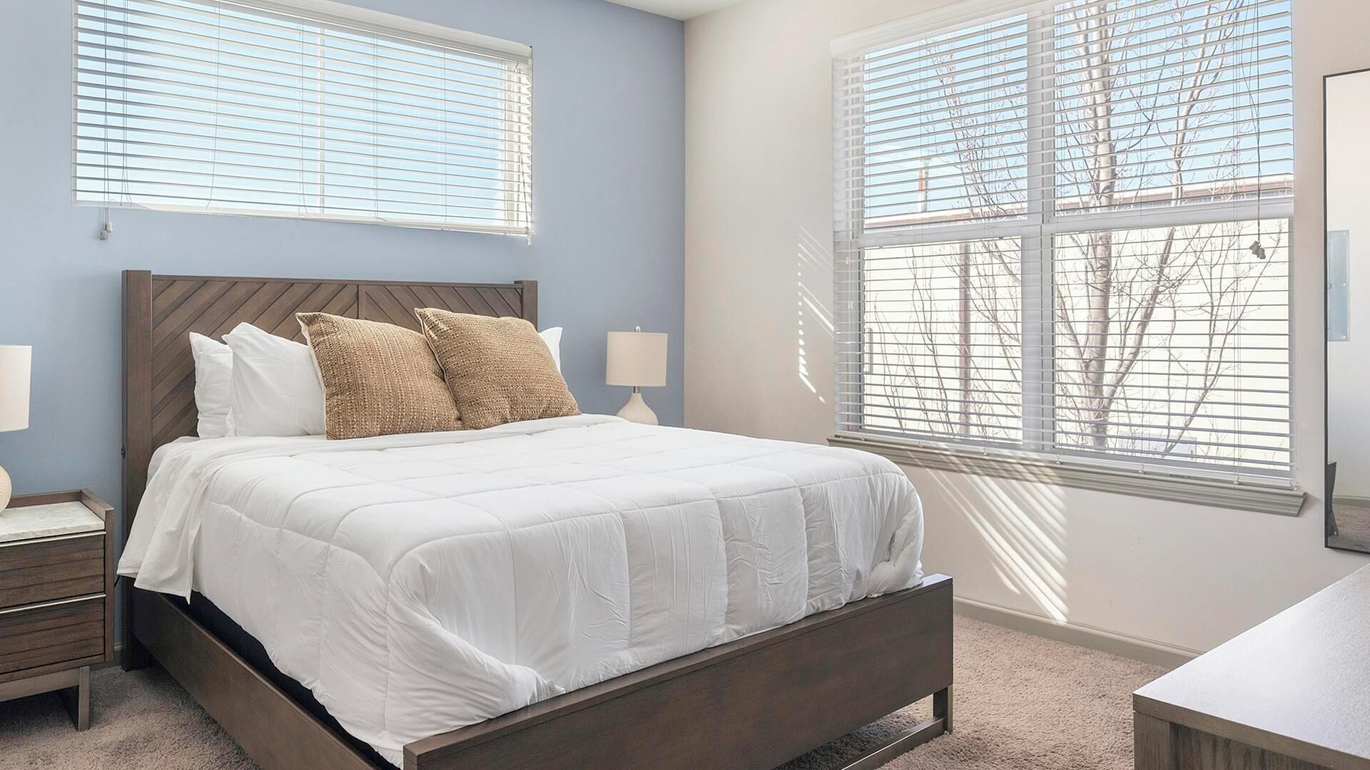 A bedroom with a bed, two bedside tables, and a window with blinds.