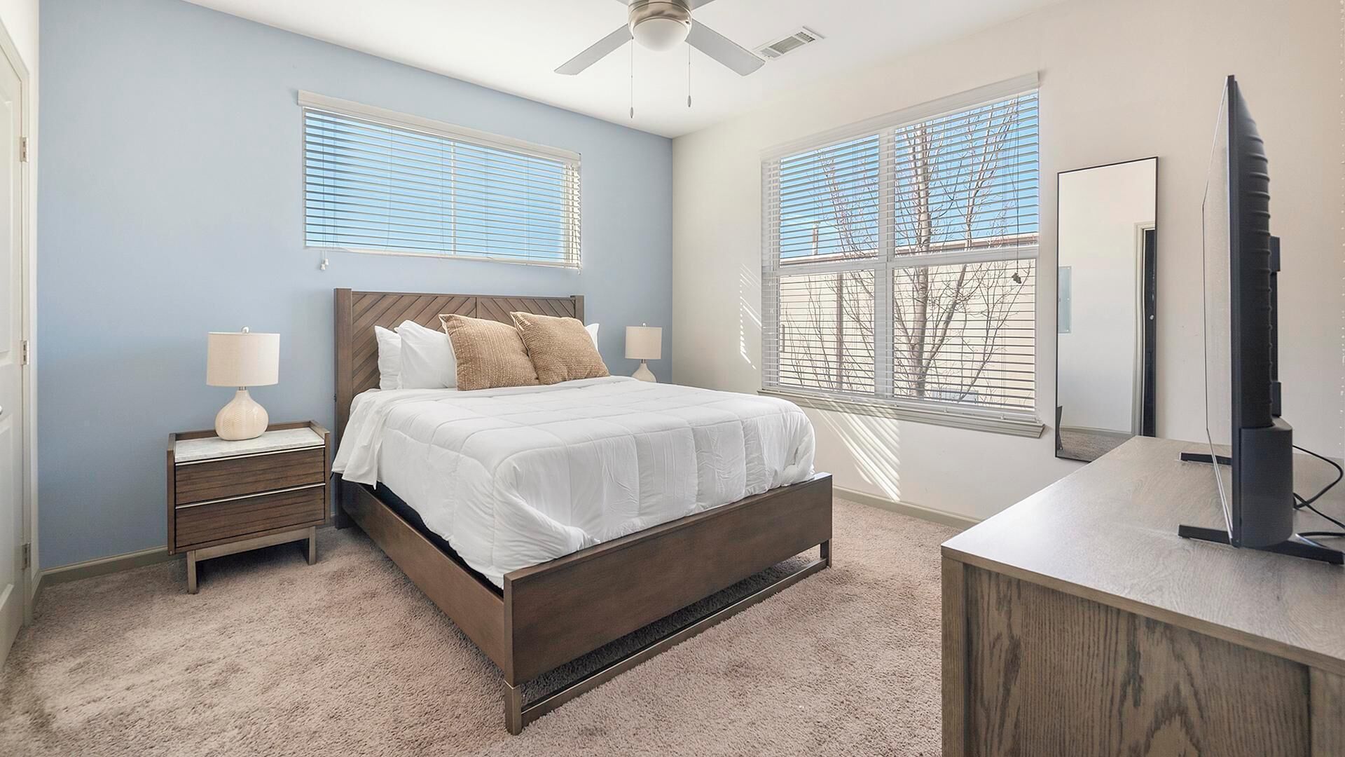 A bedroom with a bed, nightstands, a desk, and a ceiling fan.