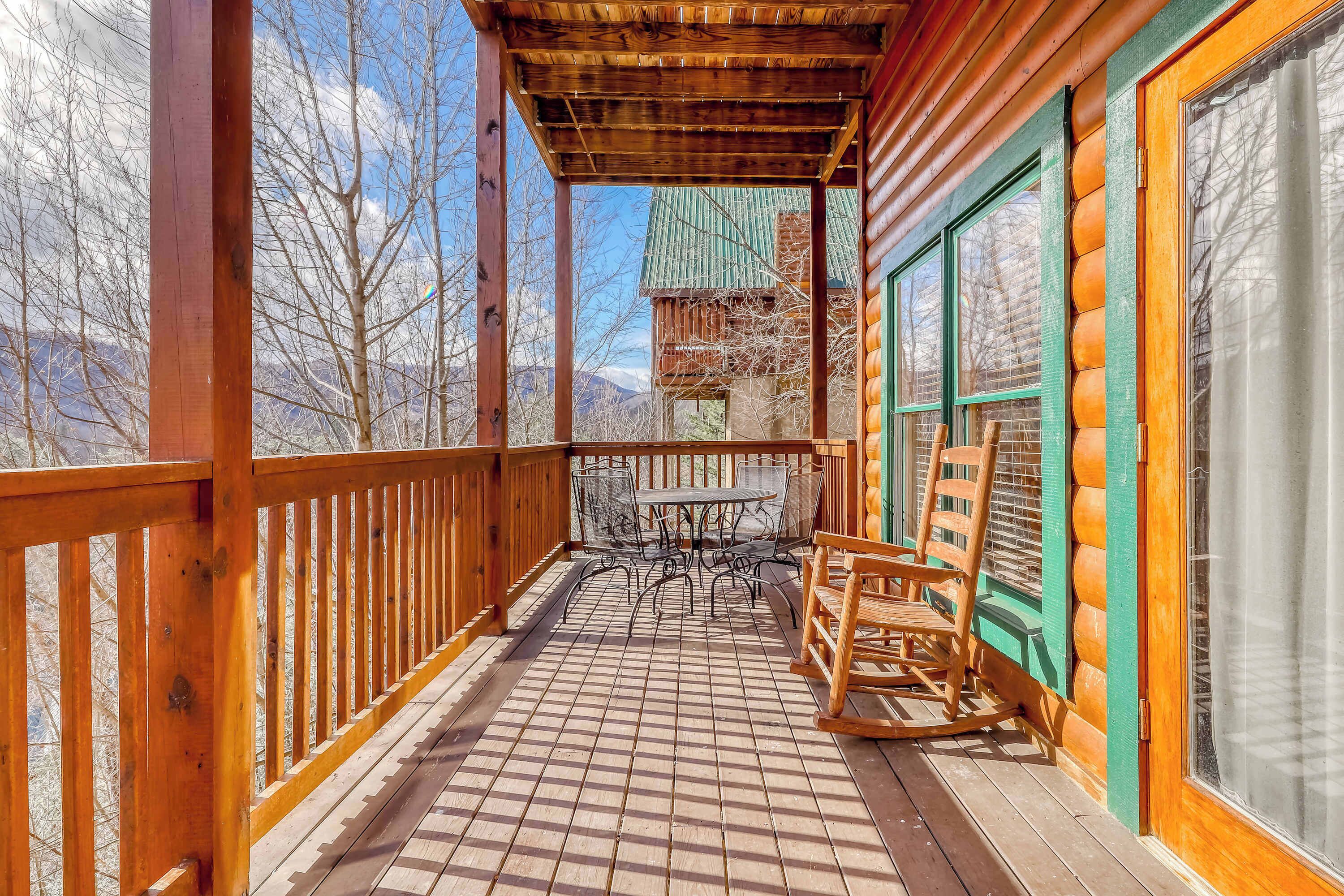 Une terrasse en bois avec une table et des chaises, un fauteuil à bascule et une vue sur un chalet de montagne.