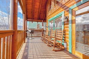 A wooden deck with rocking chairs and a grill, overlooking a mountainous landscape. - Peaceful cabin in a gated community & private hot tub (Pigeon Forge)