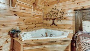 Ein Holzblockhaus-Innenraum mit einer Holzbadewanne, einer Wanddekoration aus Baum und einem Bett mit Karo-Bettwäsche.