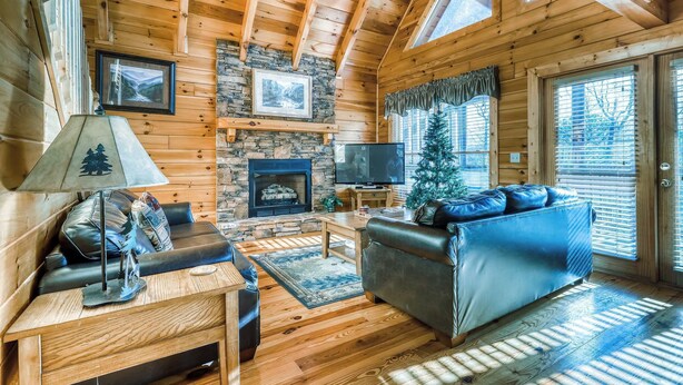 Ein gemütliches Blockhaus-Interieur mit Kamin aus Stein, Ledersofas, einem Fernseher und einem Weihnachtsbaum.