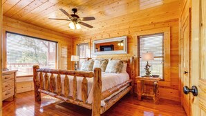 Un dormitorio de cabaña de madera con cama, ventilador de techo, televisor y dos lámparas de noche.