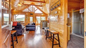 Interior de una cabaña de troncos con sala de estar, cocina y un balcón.