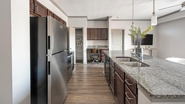 A modern kitchen with a stainless steel refrigerator, granite countertops, wooden cabinets, and a built-in oven. - Landing | Stunning 2BD, Gym, Pool (Nashville)