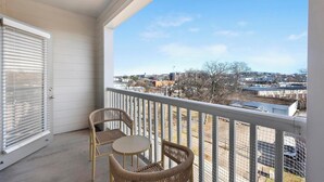 A balcony with two wicker chairs and a small table, overlooking a cityscape with buildings and trees. - Landing | Stunning 2BD, Gym, Pool (Nashville)