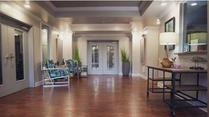 A spacious hallway with wooden flooring, a seating area with chairs, a table with a lamp, and a potted plant. - Landing | Stunning 2BD, Gym, Pool (Nashville)