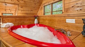 A wooden cabin interior with a red bathtub filled with ice, a towel rack with towels, a vase with flowers, and a sign on the wall. - Cabin near Dolly - Parkway・Hot Tub・Screened Porch (Pigeon Forge)