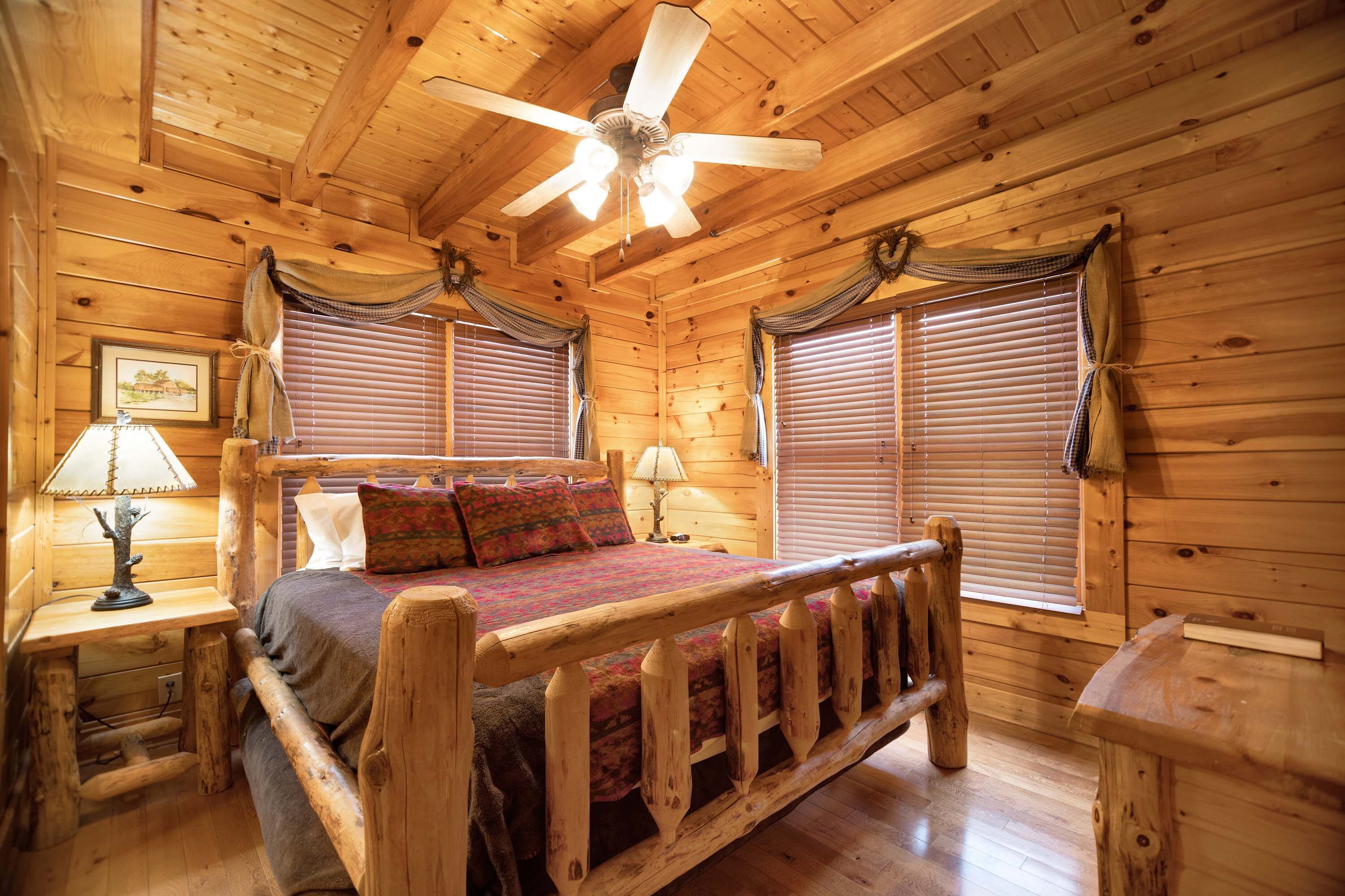 A wooden cabin bedroom with a bed, two nightstands, a ceiling fan, and wooden walls.