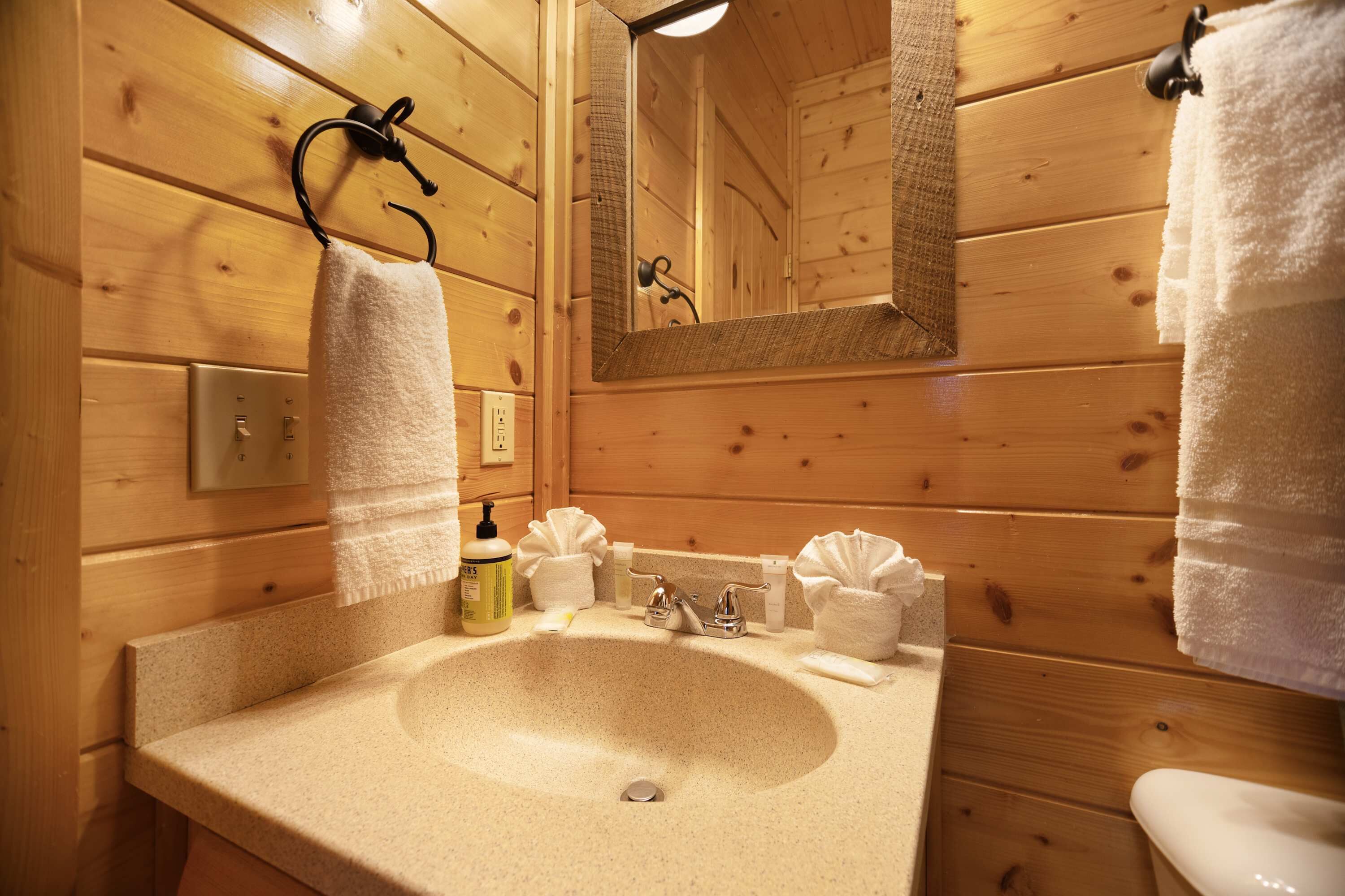 A wooden cabin bathroom with a sink, mirror, towel rack, and toilet.