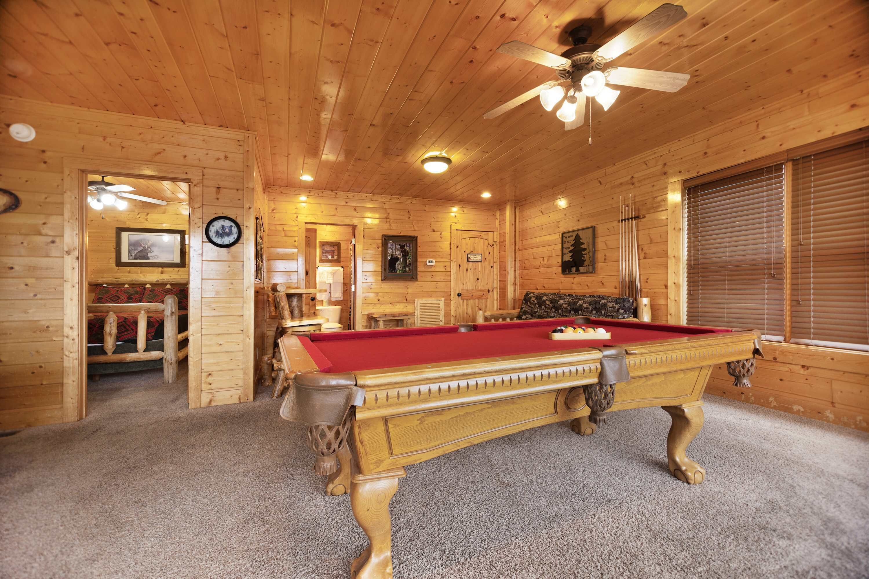 A wooden interior with a pool table, ceiling fan, and framed pictures on the walls.