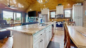 A spacious kitchen with wooden cabinets, a large island, and a dining area with a wooden table and chairs. - Luxe Mtn View Cabin, Sleep 8, Hot Tub, Games, Theater (Sevierville)