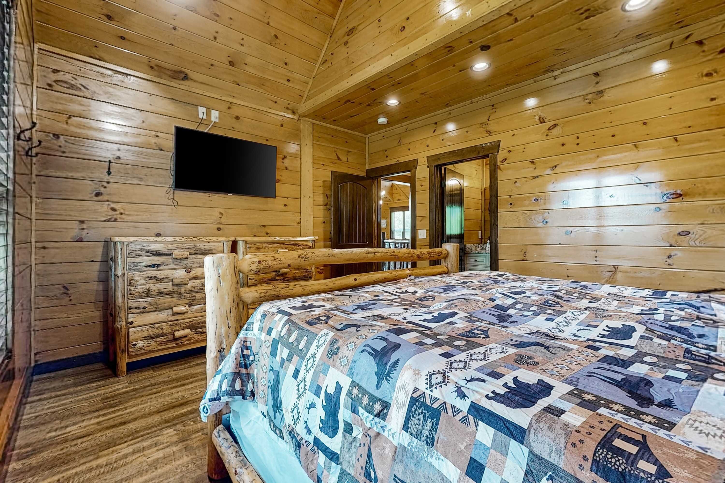 Een slaapkamer in een blokhut met een bed, houten wanden, een bevestigde televisie en een houten bank.