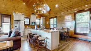 A spacious kitchen with wooden cabinets, a central island with stools, a refrigerator, and a microwave. - Luxe Mtn View Cabin, Sleep 8, Hot Tub, Games, Theater (Sevierville)