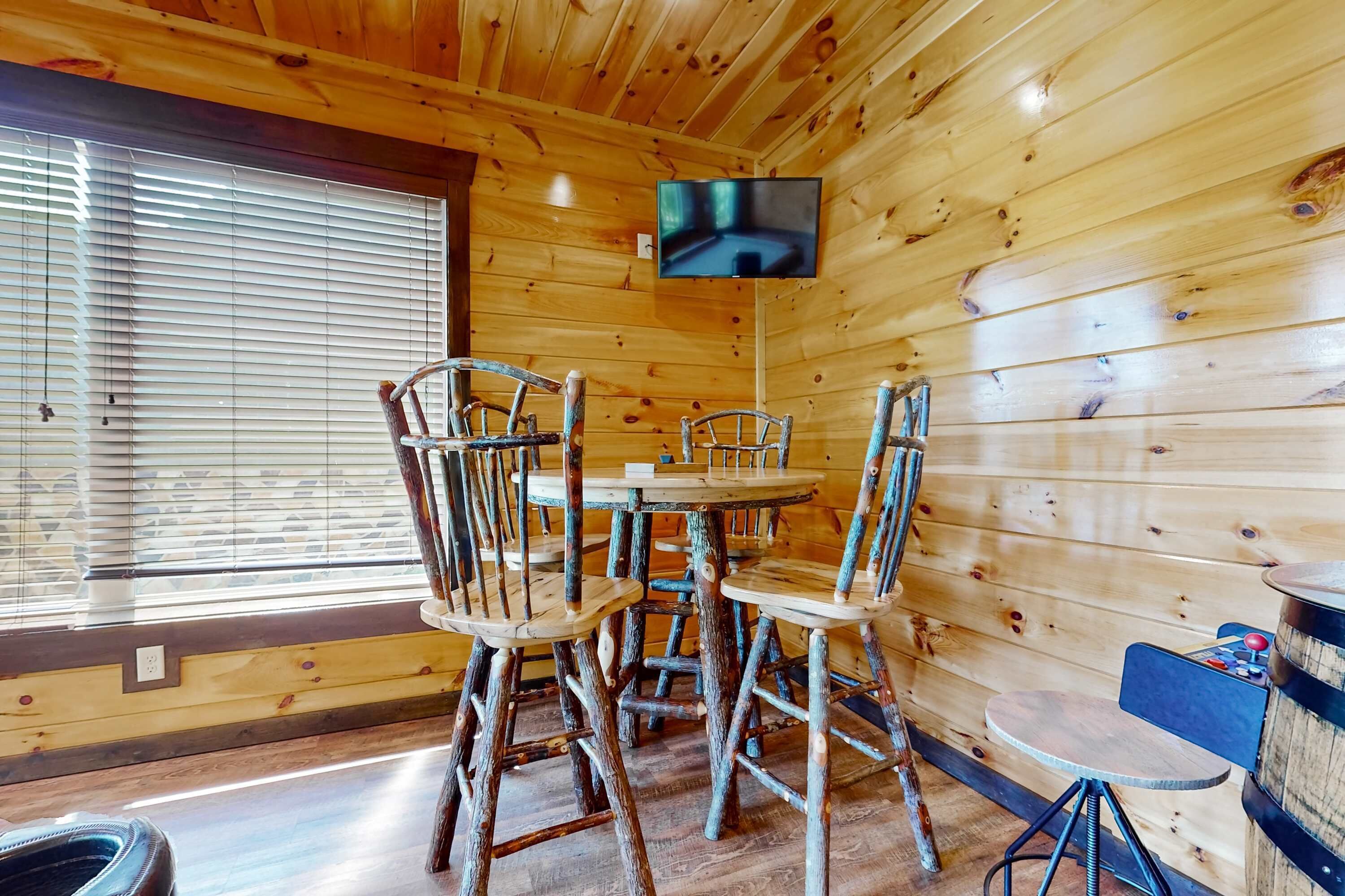 L’intérieur d’une cabane en bois, avec une table ronde et quatre chaises, un téléviseur fixé au mur, et une petite table ronde avec une chaise.