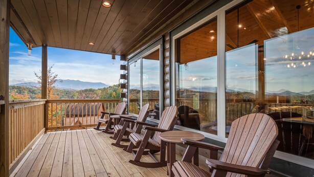A wooden deck with Adirondack chairs and a table, overlooking a mountainous landscape. - Luxe Mtn View Cabin, Sleep 8, Hot Tub, Games, Theater (Sevierville)