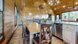 A wooden cabin interior with a dining table, chairs, a kitchen area with a dishwasher, and a ceiling fan. - Luxe Mtn View Cabin, Sleep 8, Hot Tub, Games, Theater (Sevierville)