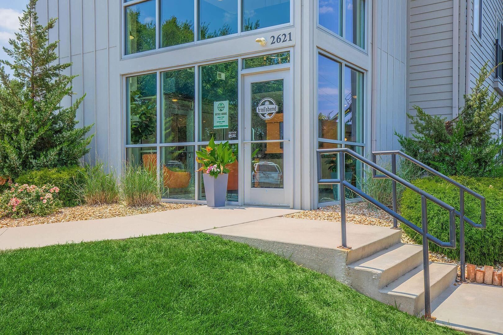A modern building with a glass entrance, a sign indicating office hours, and a number 2621.