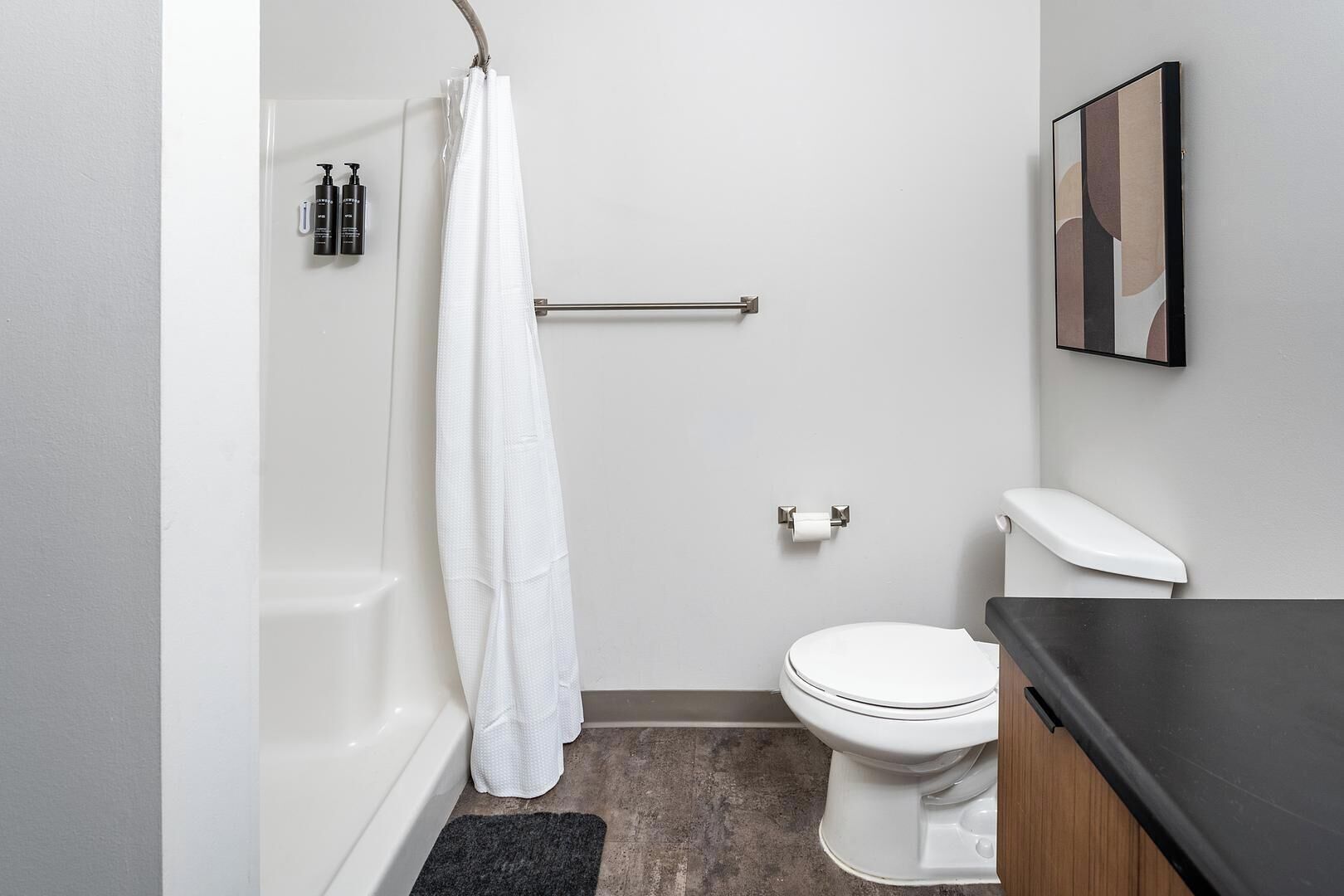 A small, modern bathroom with a white bathtub, a white toilet, and a black countertop.