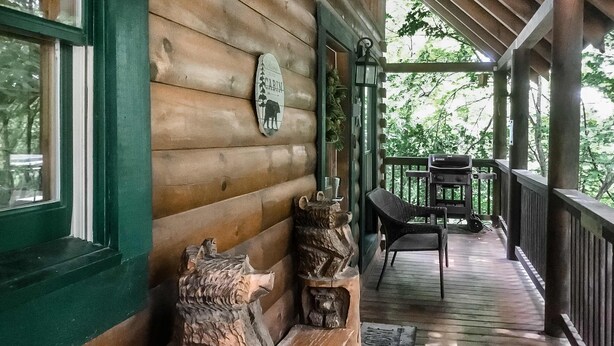Una cabaña de madera con un porche, un banco de madera, un letrero que dice "CAMPING" y una escultura de madera rústica.