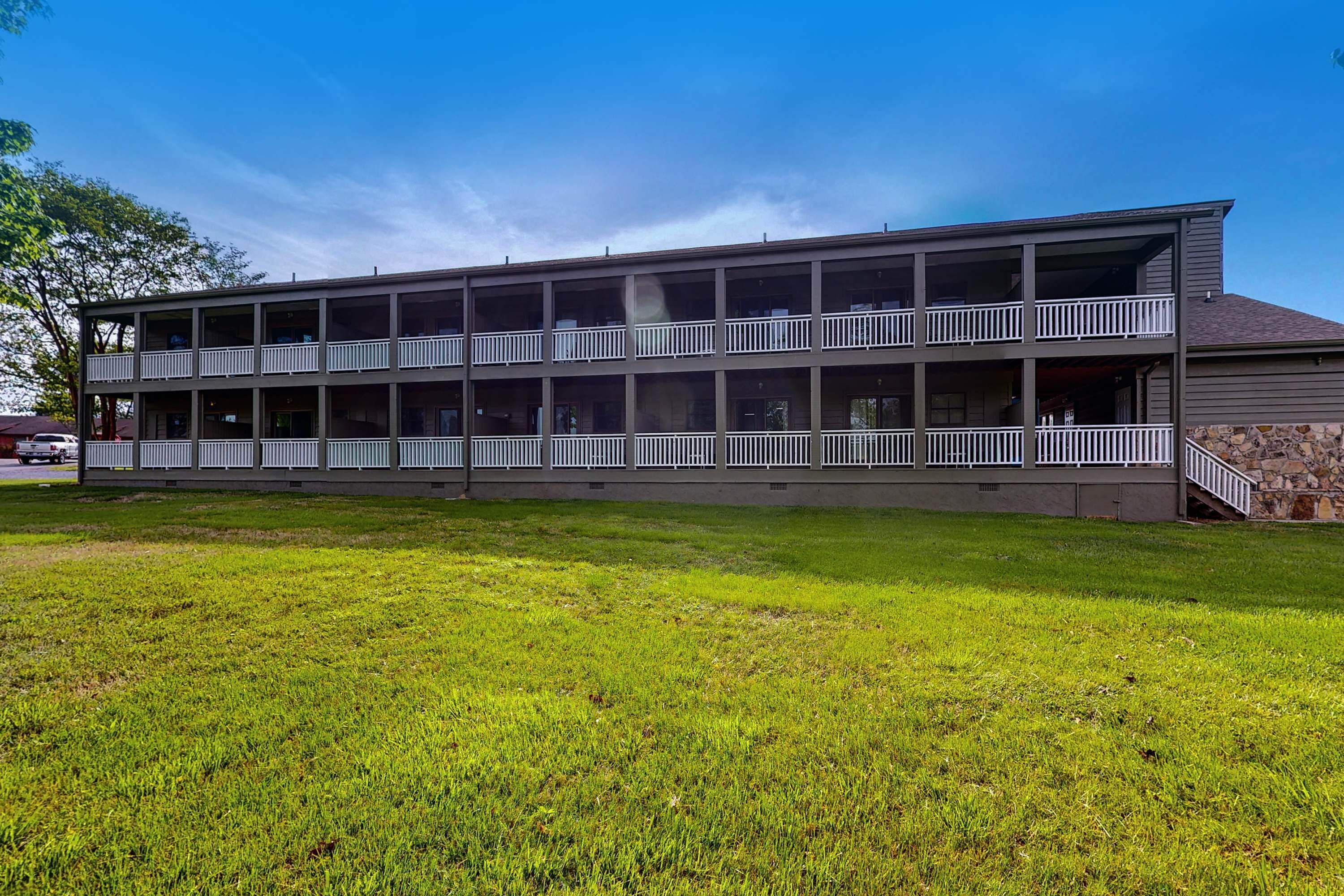 A two-story building with balconies, a stone foundation, and a grassy lawn.