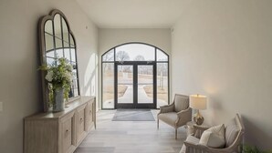 A spacious hallway with a large arched doorway, a wooden cabinet with a mirror, and a seating area with a lamp. - Landing | Incredible 3BD, Pool, Gym (Sapulpa)