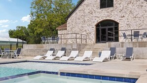 A swimming pool with lounge chairs and a stone building with a large arched entrance. - Landing | Incredible 3BD, Pool, Gym (Sapulpa)