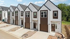 A row of modern, two-story townhouses with white and brown exteriors, garage doors, and a clear sky. - Landing | Incredible 3BD, Pool, Gym (Sapulpa)
