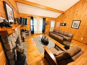 A cozy cabin interior with a stone fireplace, leather sofa, and a flat-screen TV mounted on the wall. - Pigeon Forge Cabin on the Creek | 4 Min to Strip (Pigeon Forge)