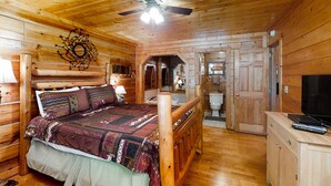 L’intérieur d’un chalet en bois, avec un lit, un ventilateur de plafond, un téléviseur et une salle de bain visible à travers une porte ouverte.