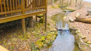 Une terrasse en bois surplombant un ruisseau, avec des rochers et des feuilles.
