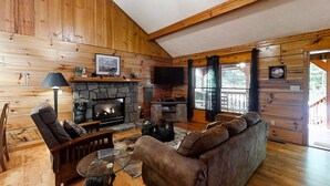 L’intérieur d’un chalet confortable, avec une cheminée en pierre, des murs en bois, un canapé confortable et un téléviseur.