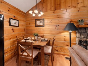 A wooden interior with a dining table set for four, a black lamp, and framed pictures on the walls. - Cozy Creekside Cabin Near Pigeon Forge | Sleeps 4 (Pigeon Forge)