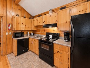 A compact kitchen with wooden cabinets, a black refrigerator, a microwave, a stove, and a coffee maker. - Cozy Creekside Cabin Near Pigeon Forge | Sleeps 4 (Pigeon Forge)