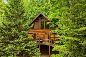 Une cabane en rondins dotée d’un balcon, entourée d’une forêt dense.