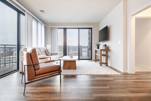 A spacious living room with a sofa, a coffee table, and a TV mounted on the wall. - Landing | Spectacular 2BD, Gym, Courtyard (Milwaukee)