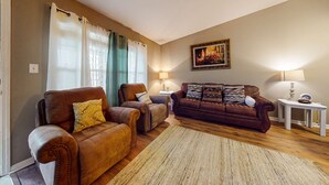 Ein Wohnzimmer mit braunem Ledersofa, zwei Sesseln, Holzboden und Teppich.