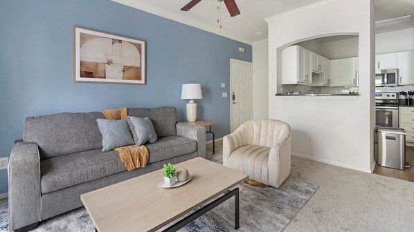 A living room with a grey sofa, a beige armchair, a coffee table, and a painting on the wall. - Landing | Stylish 1BD, Gym, Clubhouse (Jacksonville)
