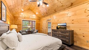 Ein Schlafzimmer einer Holzhütte mit Bett, Schminktisch, Fernseher und einem Fenster mit Buntglas.