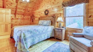 Ein Schlafzimmer einer Holzhütte mit Bett, Nachttisch, Lampe und Fenster.